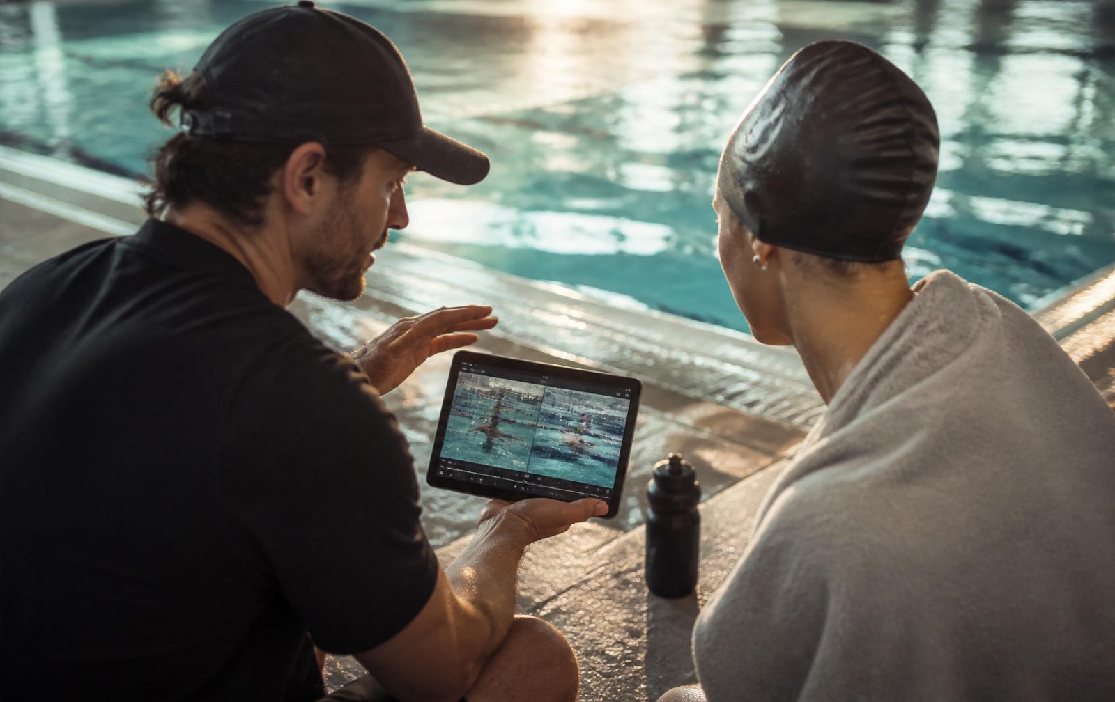 Swim coach reviewing video analysis on a tablet with a swimmer poolside