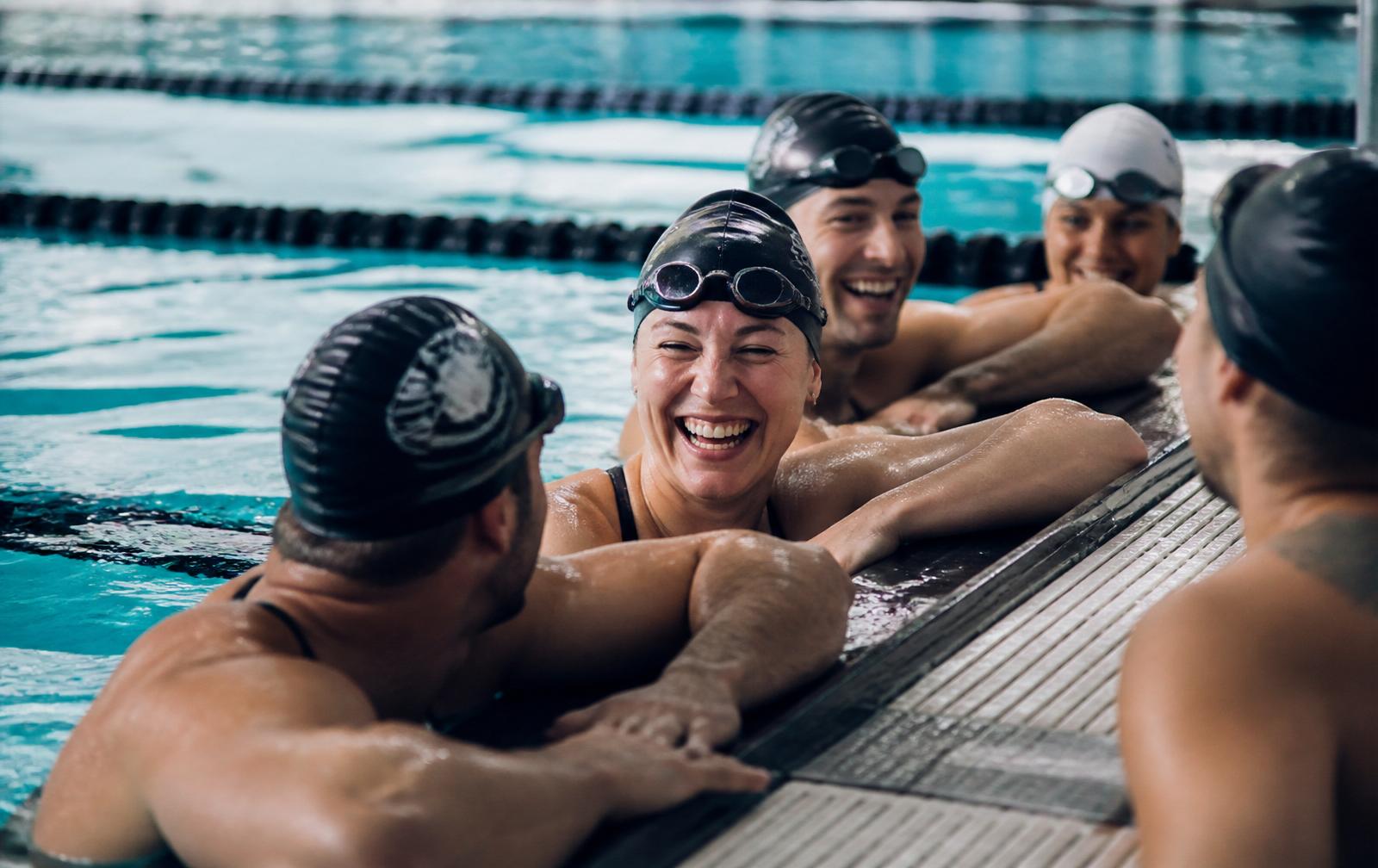 Squad of adult swimmers laughing together at the end of a lane