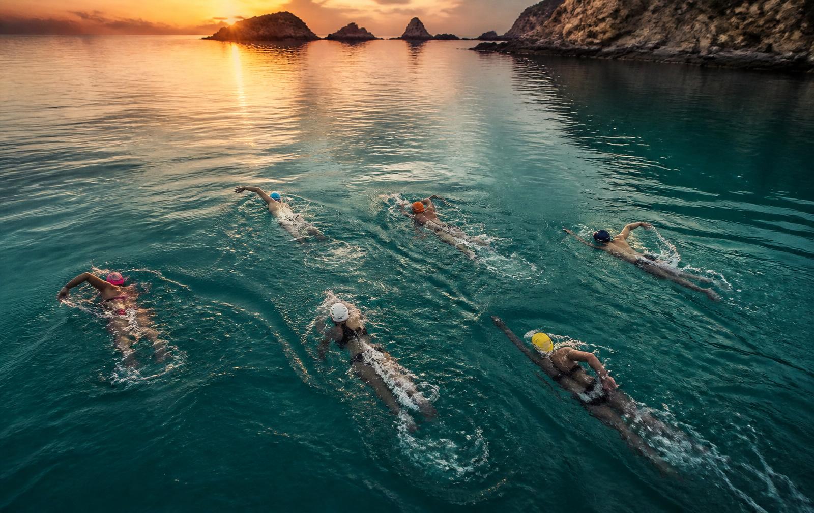 Aerial view of six open-water swimmers with different strokes at sunrise